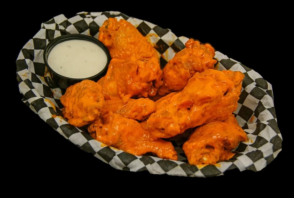 A basket of sauced jumbo wings with a dipping cup on checkered paper